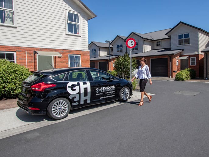 Hamilton property management agent walking to a car with Glasshouse written on it after completing a property inspection.
